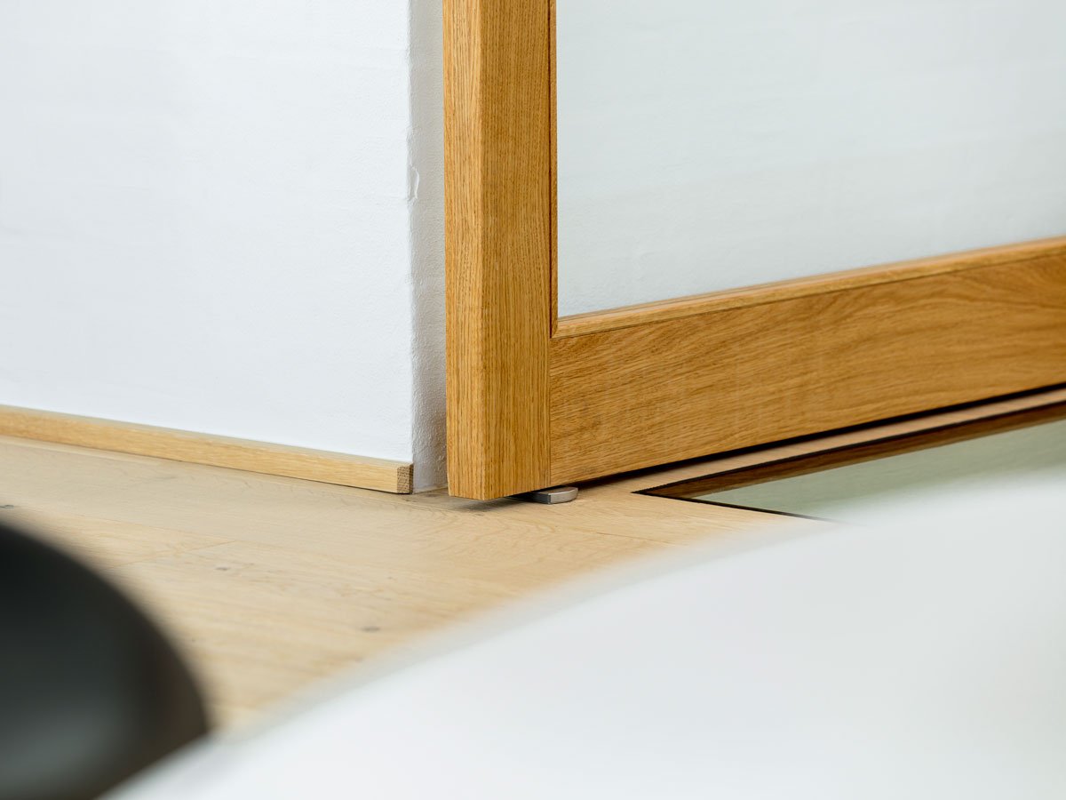 Eine FritsJurgens Bodenplatte aus rostfreiem Edelstahl unter einer Pivot Tür. Auf der Bodenplatte liegend, ist das Pivot Scharnier im Holz-Türrahmen versteckt.